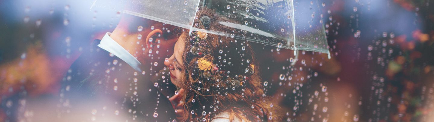 a bride and groom kiss in the rain under an umbrella
