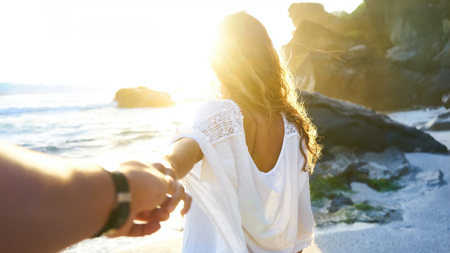 person holding woman's hand beside sea while facing sunlight